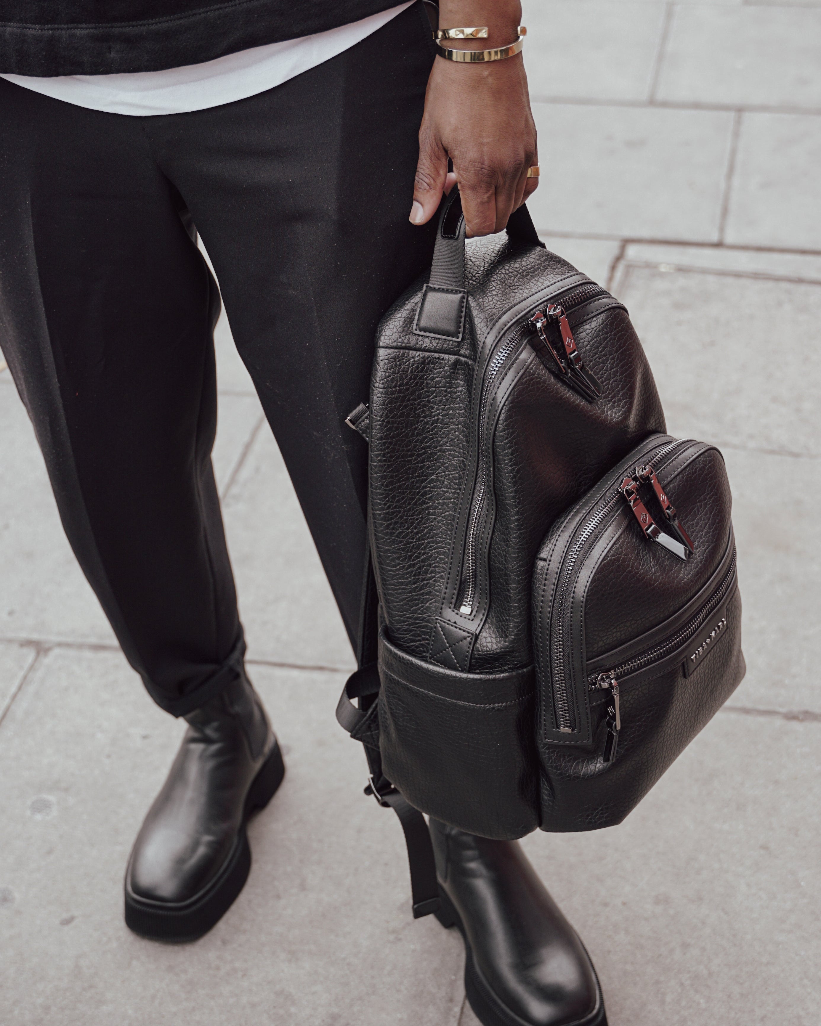 Person holding a black leather backpack on a pavement background