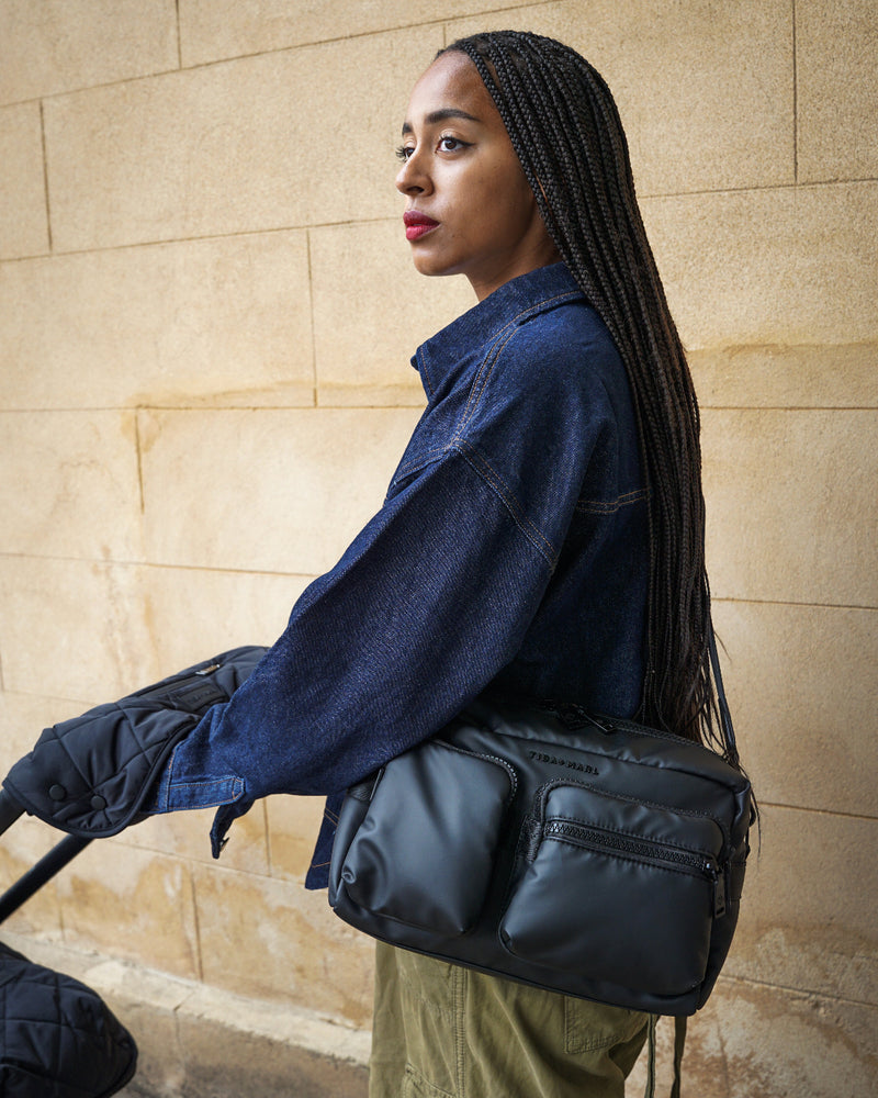 Woman holding a black bag against a beige wall
